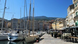 A marina with boats docked, a waterfront promenade, and buildings in the background.