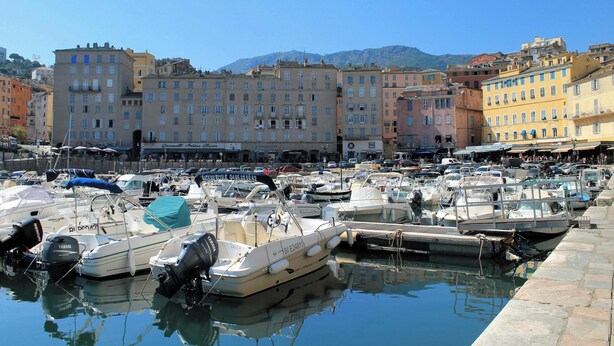 A marina with boats docked, buildings in the background, and a clear sky.