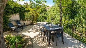 An outdoor patio with a table and chairs, surrounded by greenery and a fence.