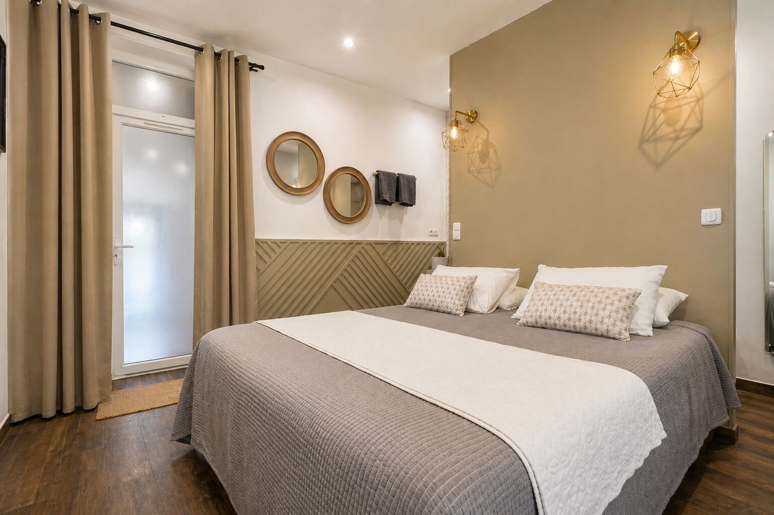 A bedroom with a bed, curtains, a wall-mounted mirror, and a wall light fixture.