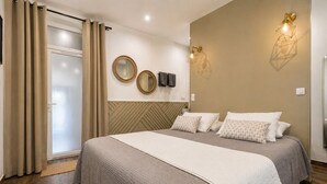 A bedroom with a bed, curtains, a wall-mounted mirror, and a wall light fixture.