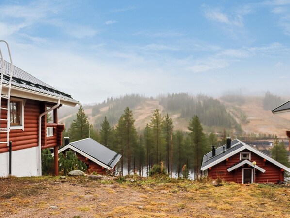 A cabin with a metal roof and a wooden exterior, surrounded by a forest and a lake.