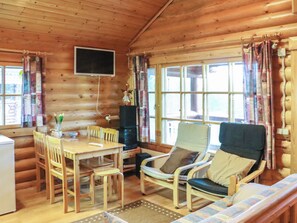 A cozy cabin interior with a wooden dining table, chairs, a sofa, and a television mounted on the wall.
