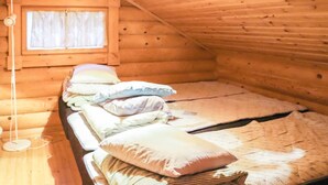 Un dormitorio rústico de cabaña de madera con una cama individual, almohadas, una lámpara de noche y una ventana con cortinas.