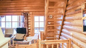 Interior de una cabaña de madera con sofá, sillones, un escritorio y una escalera.