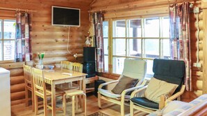 Interior acogedor de una cabaña con paredes de madera, una mesa de comedor con sillas, un sofá y un televisor montado en la pared.