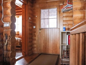 L’intérieur d’une cabane en bois, avec une porte, une fenêtre avec des rideaux, une étagère avec divers objets et un porte-manteau suspendu.