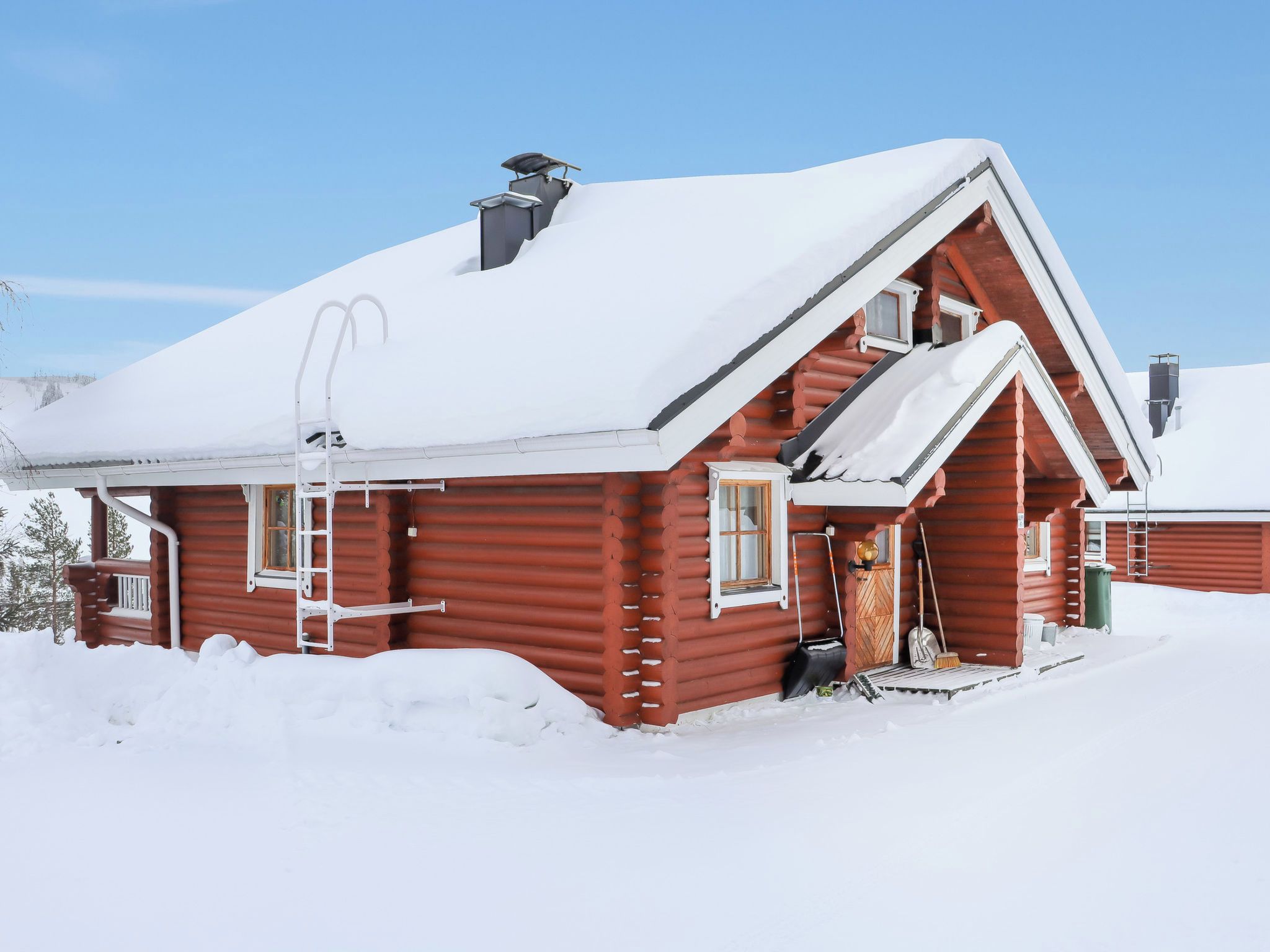 Eine Blockhütte mit einem steilen Walmdach, einer Leiter und einer schneebedeckten Fassade.