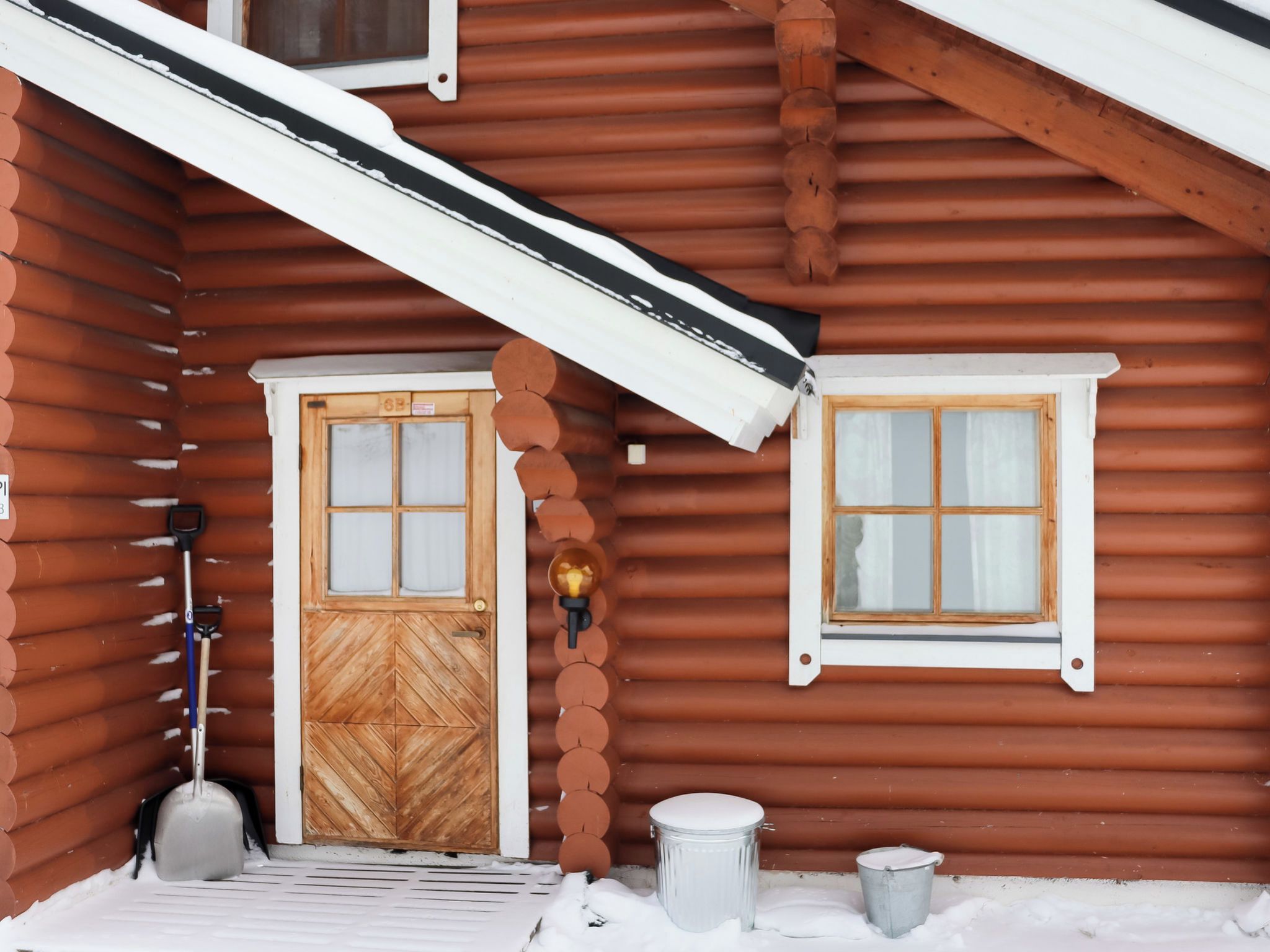 Eine Holzhütte mit einem verschneiten Veranda, einer Tür und einem Fenster.