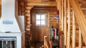 A log cabin interior with a fireplace, wooden staircase, and a small shelf with items. - Alppi 6b paritalo by Interhome (Hyrynsalmi)