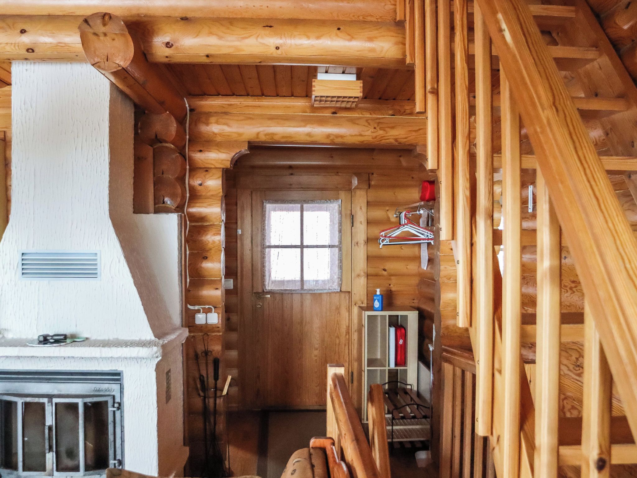 A log cabin interior with a fireplace, a wooden staircase, and a window.