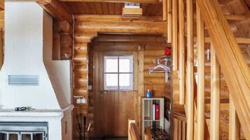 A log cabin interior with a fireplace, a wooden staircase, and a window.