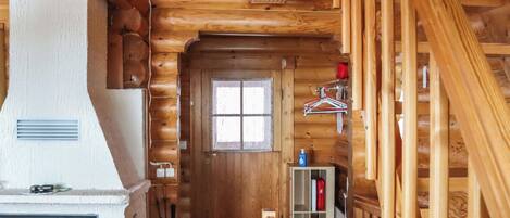 A log cabin interior with a fireplace, a wooden staircase, and a window.