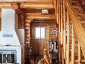 L’intérieur d’une cabane en rondins, avec une cheminée, un escalier en bois et une fenêtre.