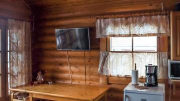 A cabin interior with a wooden dining table, bar stools, a television mounted on the wall, a refrigerator, and a coffee maker.