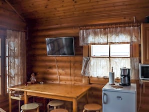 L’intérieur d’une cabine comprenant une table à manger en bois, des tabourets de bar, un téléviseur fixé au mur, un réfrigérateur et une machine à café.