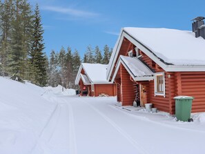 Une cabane en bois recouverte de neige, avec un ciel dégagé, entourée d’arbres.