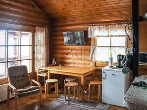 L’intérieur chaleureux d’un chalet avec une table à manger en bois, des chaises, un téléviseur fixé au mur et un petit réfrigérateur.