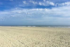 A wide sandy beach with visible tire tracks leading to the water.