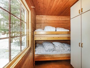 A cabin with a bunk bed, wooden walls, and a window overlooking a snowy landscape.