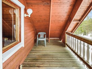 A wooden balcony with a chair, a window, and a railing.