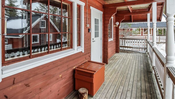 Een houten veranda met een witte balustrade, een bank en een deur.