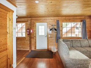 A log cabin interior with a sofa, a door, a window, and a fire extinguisher.