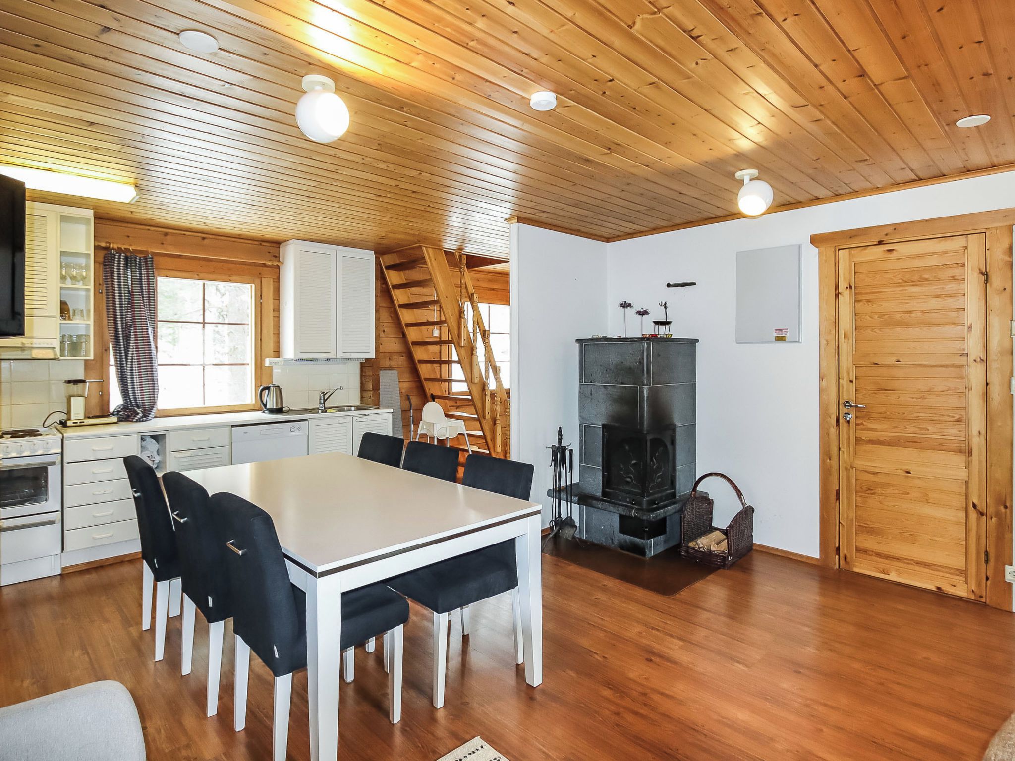 Une cuisine moderne avec des meubles blancs, une table à manger avec des chaises, une cheminée et un escalier en bois.