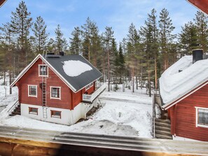 Une cabane rouge avec un porche, entourée d’un paysage enneigé et de grands pins.