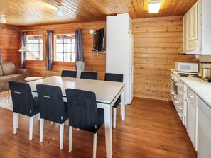 L’intérieur d’un chalet en bois comprend une table à manger, des chaises, un coin cuisine équipé d’appareils électroménagers et un canapé.