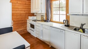 Een compacte keuken met houten wanden, witte kasten, een magnetron, een waterkoker en een spoelbak.