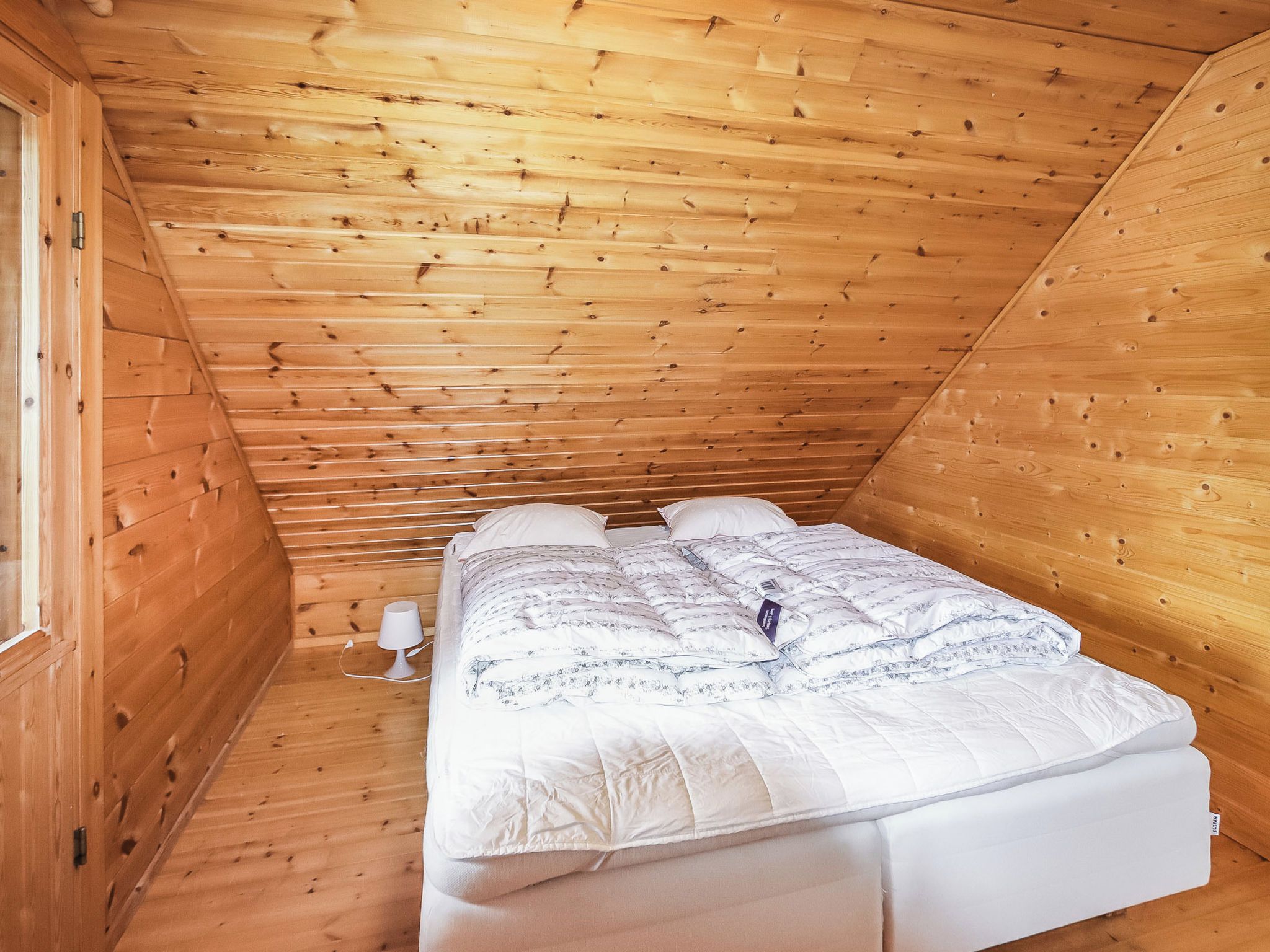 A single bed in a wooden room with a sloped ceiling.