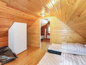 A small, wooden-paneled room with a single bed, a white wardrobe, and a door leading to another room.