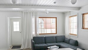 Een moderne woonkamer met een grijze bank, een witte tafel en een raam met zonwering.