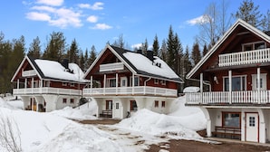 Een chalet met een balkon, omgeven door sneeuw en bomen.