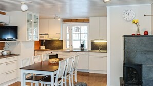 A modern kitchen with white cabinets, a dining area with a wooden table and white chairs, a television, and a fireplace.
