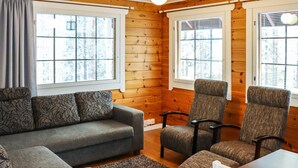 A cozy cabin interior with a sofa, two armchairs, a small table, and a rug.