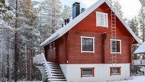 A red wooden house with a white exterior, a set of stairs leading to a porch, and a ladder on the side.