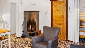 A cozy room with a fireplace, a wooden door, a dining table with chairs, and a patterned floor. - Alppikylä 8b by Interhome (Hyrynsalmi)