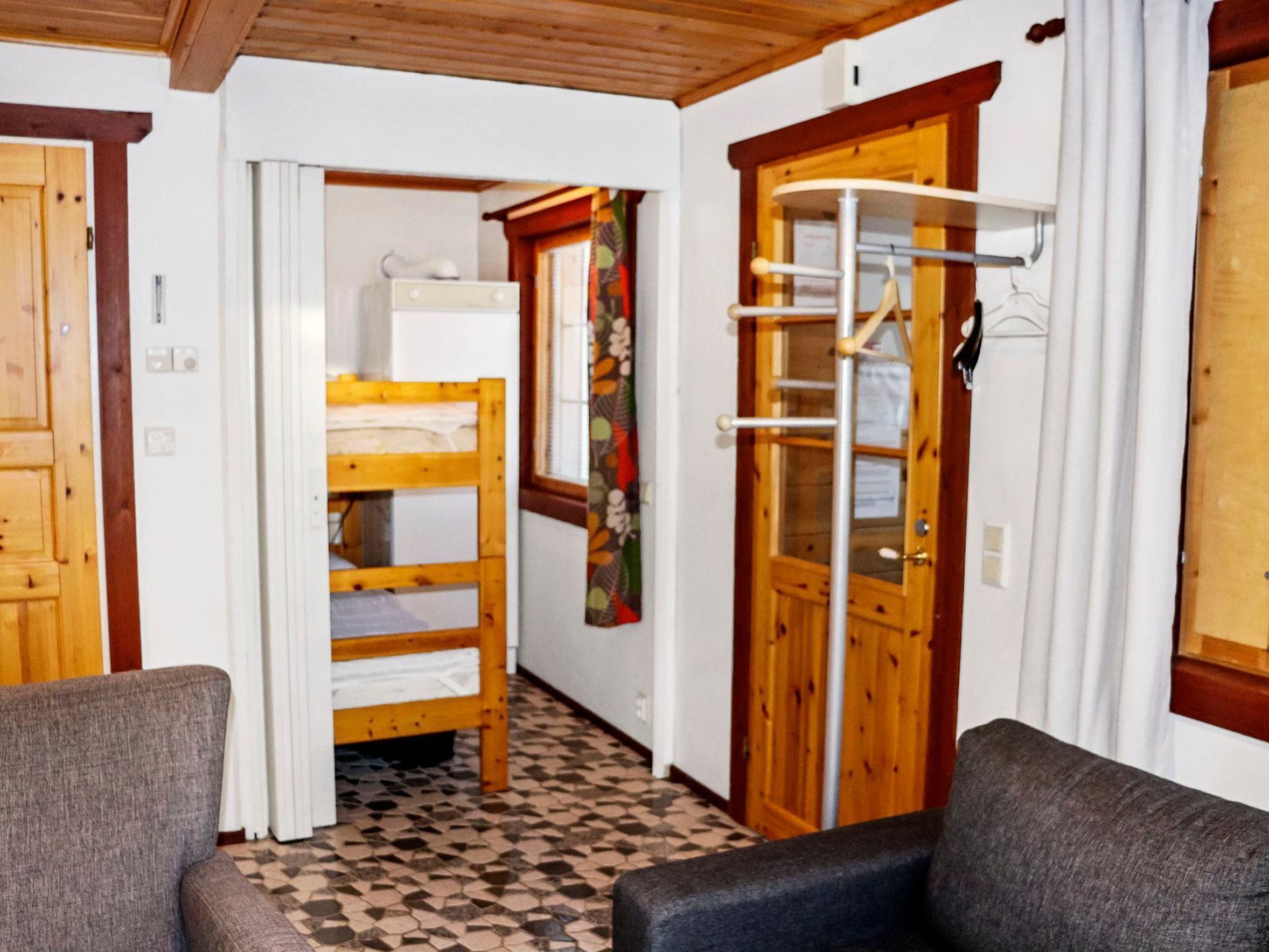 A room with a bunk bed, a wooden door, a coat rack, and a tiled floor.