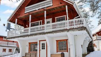 Un chalet a due piani con un balcone, facciata in legno e paesaggio innevato.