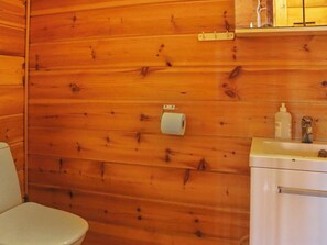 Baño de cabaña de madera con inodoro, lavamanos y un rollo de papel higiénico en la pared.