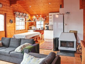 A cozy cabin interior with a sofa, a dining table, a kitchen area, and a wood-burning stove. - Alppitalo mökki by Interhome (Hyrynsalmi)