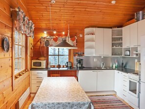 A cozy cabin-style kitchen with wooden walls, a dining table, and modern appliances. - Alppitalo mökki by Interhome (Hyrynsalmi)