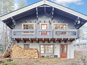 Ein zweistöckiges Holzhaus mit einem Balkon, einem Holzstapel und einer hölzernen Bank.