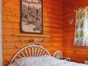Een houten kamer met een bed, een wandplank en een raam met gordijnen.