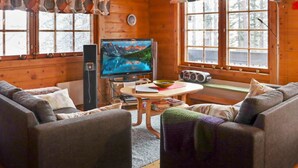 L’intérieur chaleureux d’un chalet avec des murs en bois, un téléviseur, une table avec des livres et deux canapés.