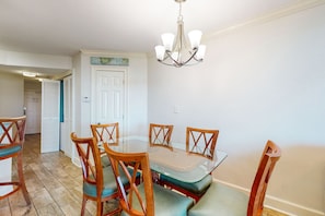 A dining area with a glass table and wooden chairs, a chandelier, and a door with a sign above it.