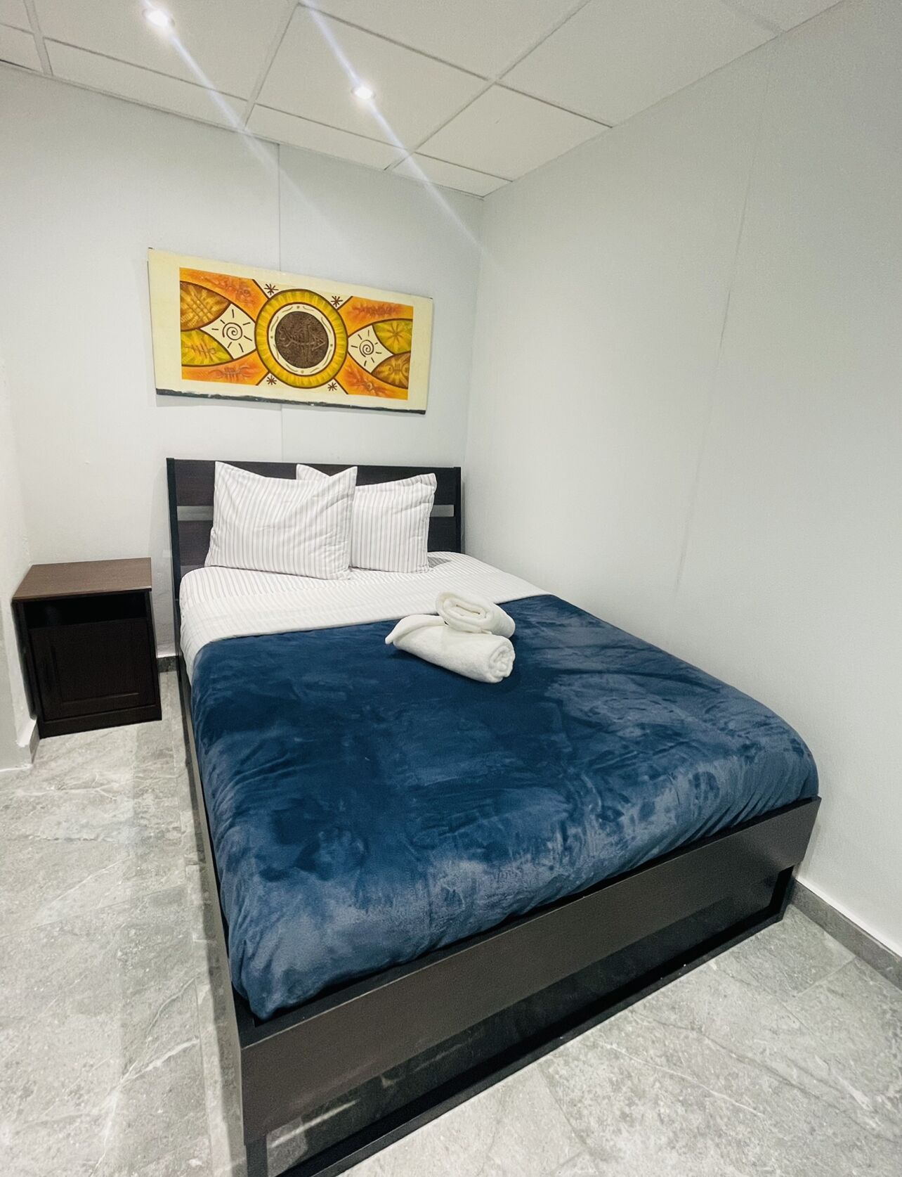 A modern bedroom with a large bed, a nightstand, and a wall-mounted artwork.
