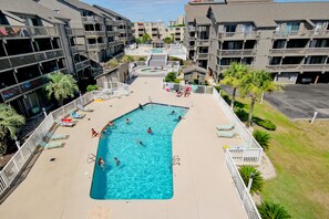 Uma piscina cercada por espreguiçadeiras e um deck, com um edifício de vários andares ao fundo.